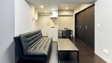 A modern living room with a black leather sofa, a small table, and a dining area with a table and chairs.