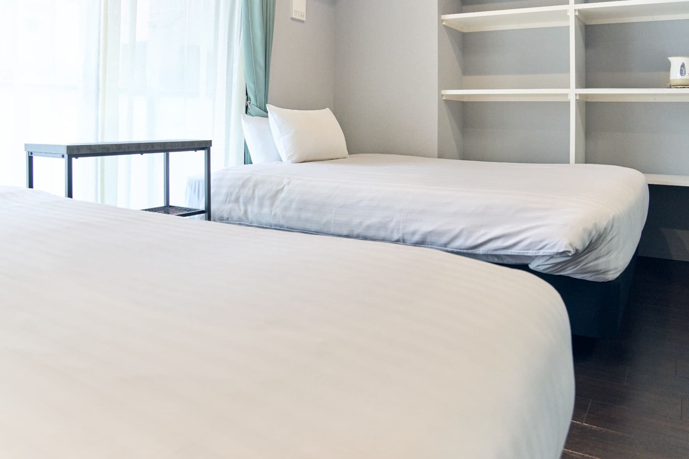 Een hotelkamer met twee bedden, een tafeltje en een inbouwkast.