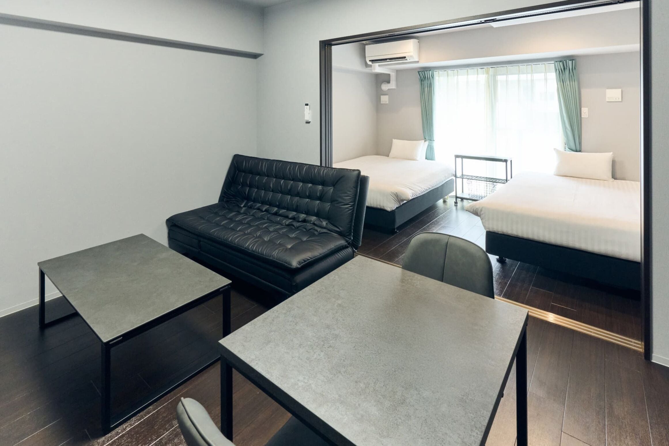 Een moderne hotelkamer met een sofa, twee tafels, een bed en een raam met gordijnen.