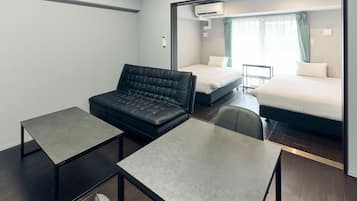 Een moderne hotelkamer met een sofa, twee tafels, een bed en een raam met gordijnen.