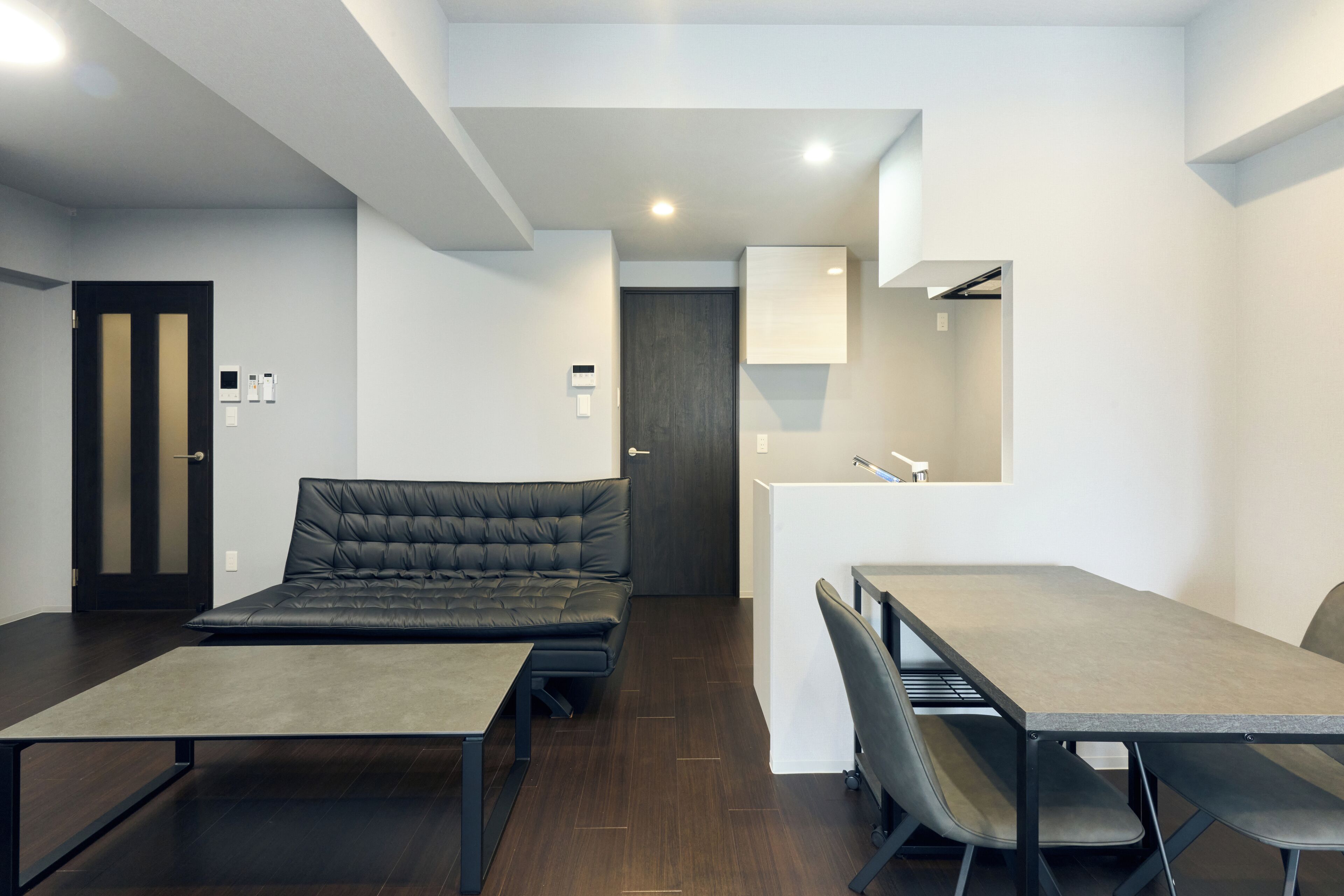 A modern, compact room with a sofa, a small table, and a desk with chairs.