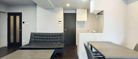 A modern, compact room with a sofa, a small table, and a desk with chairs.