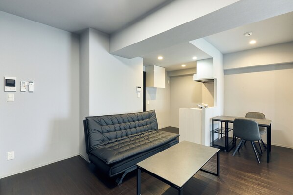 Una sala de estar moderna y minimalista con un sofá de cuero negro, una mesita y una zona de comedor con una mesa y sillas.