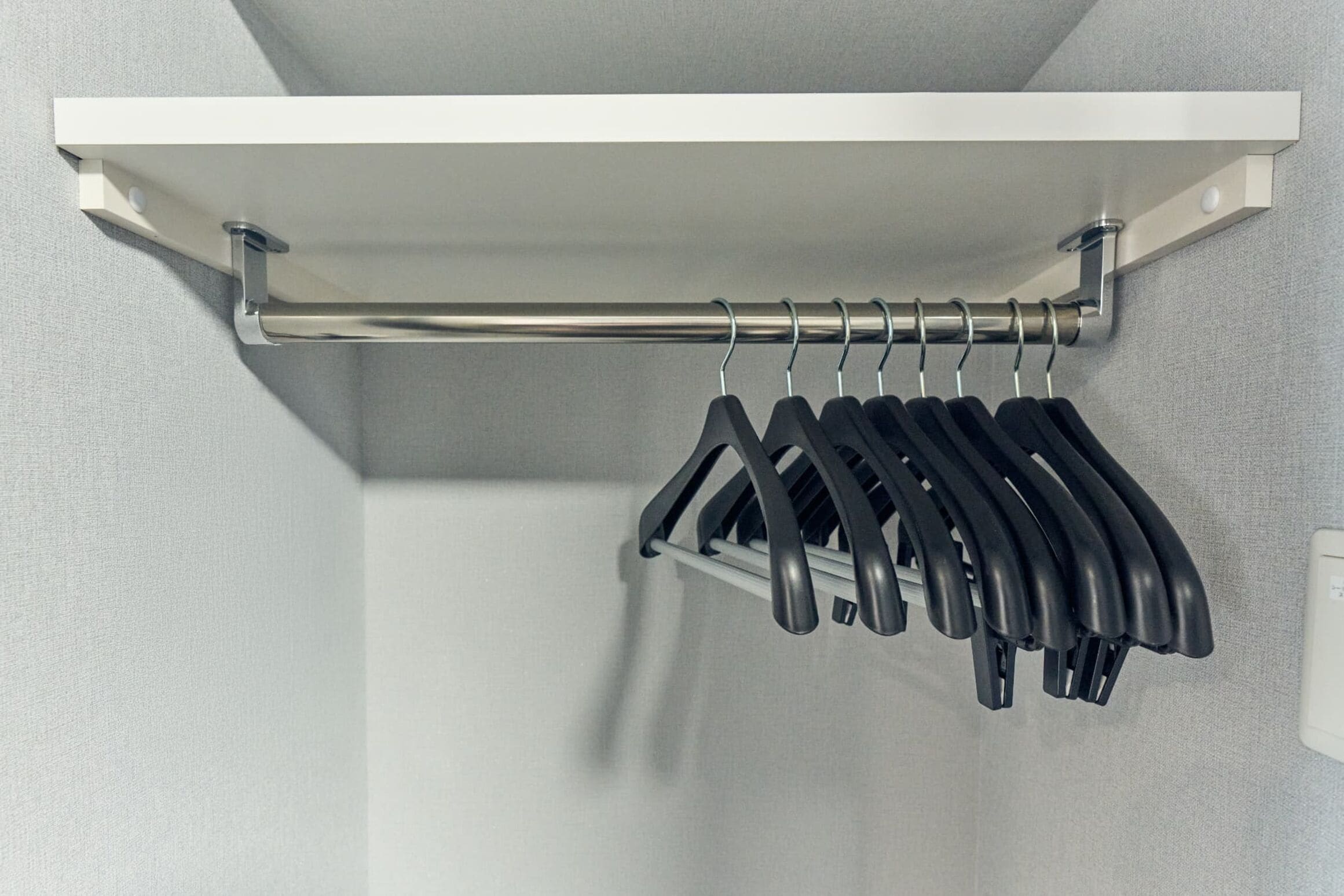 A metal rack with black hangers in a bathroom.
