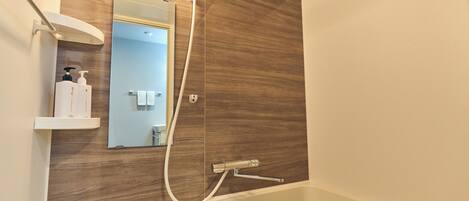 A modern bathroom with a wooden wall, a built-in shelf with toiletries, a mirror, and a bathtub.