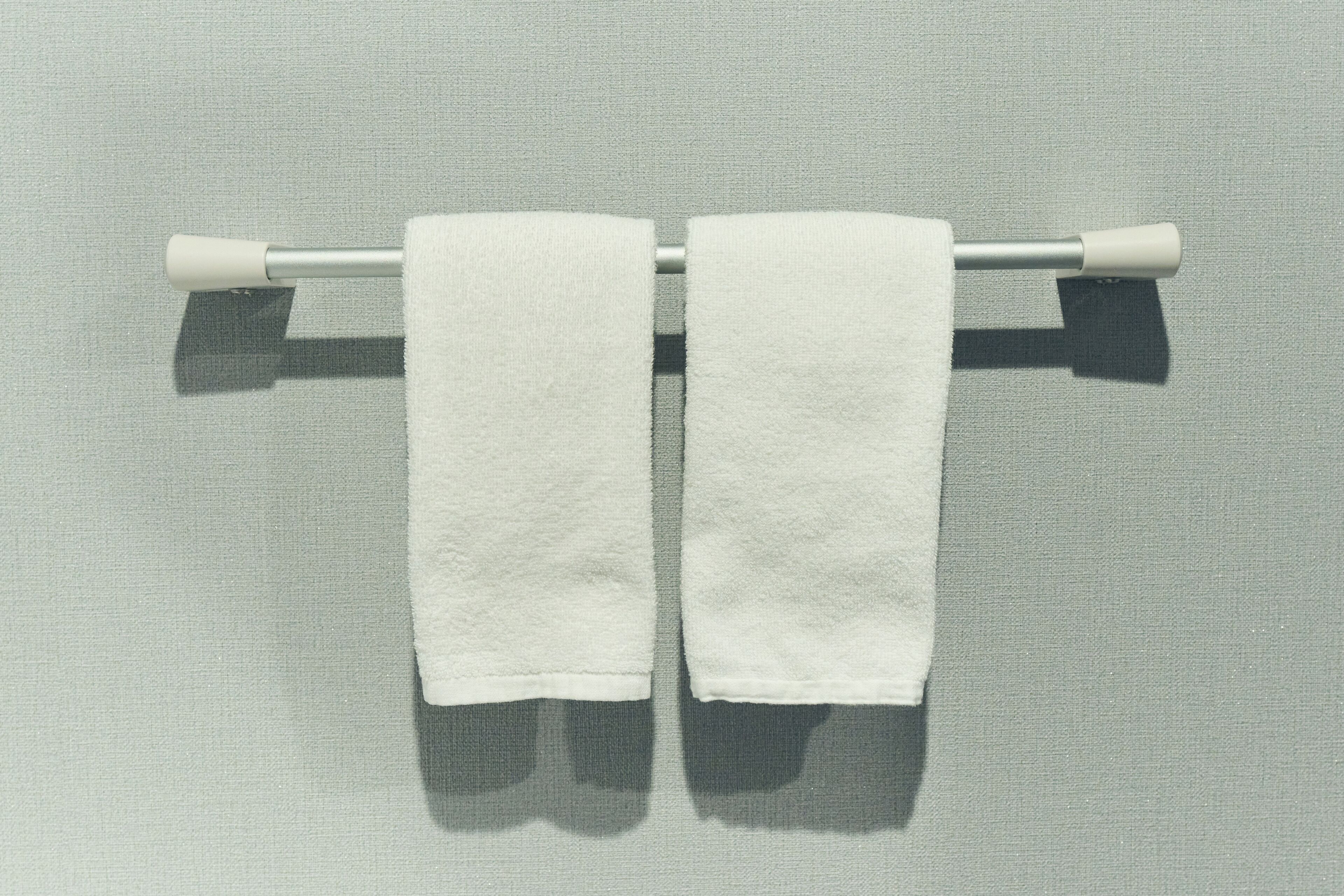 Deux serviettes blanches sont suspendues à une barre à serviettes en métal, le tout se détachant sur un mur à texture.
