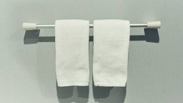 Two white towels hanging on a metal towel bar against a textured wall.