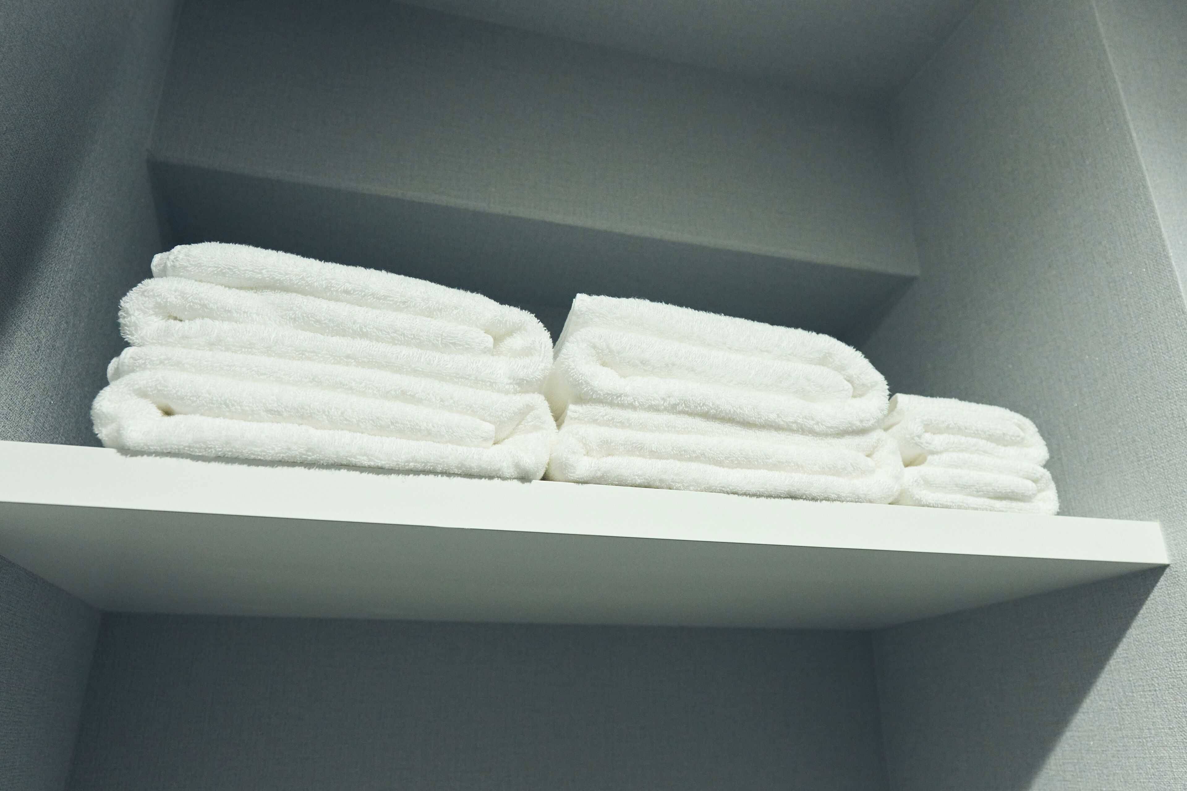 A white shelf with neatly folded white towels.
