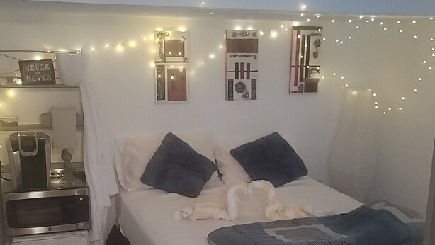 A bedroom with a bed, bedside tables, a desk, and string lights.