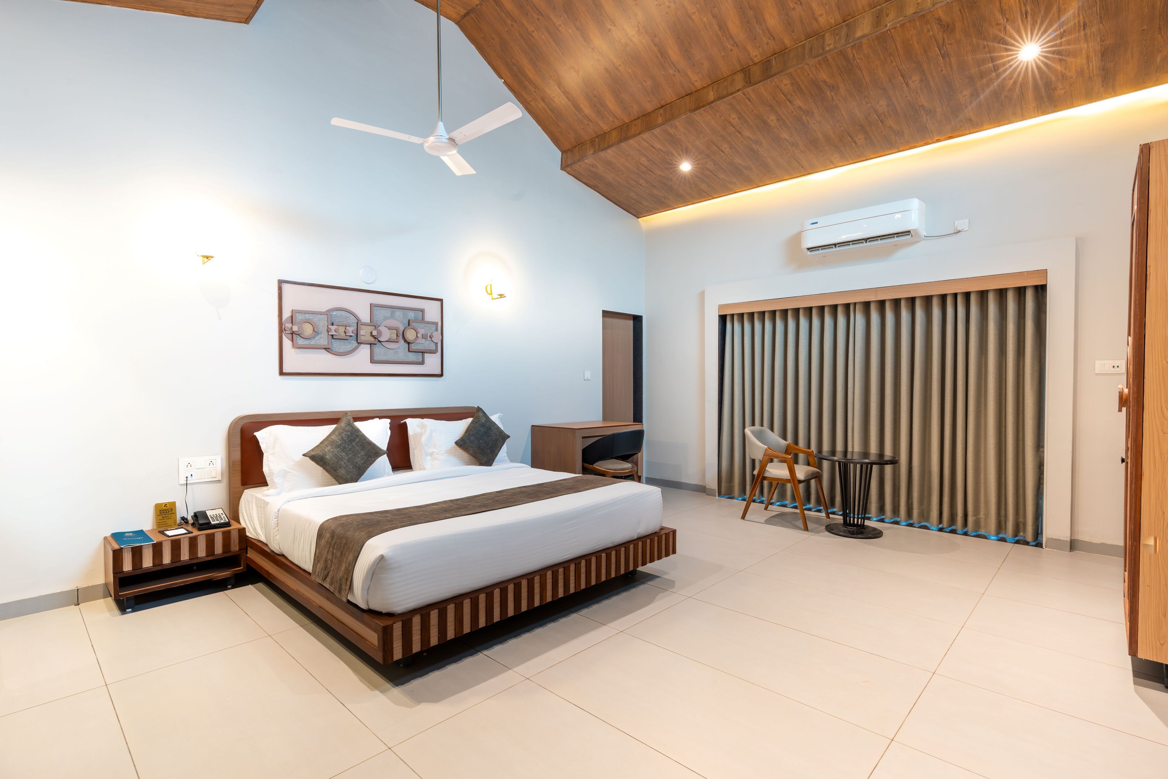 A modern hotel room with a large bed, bedside table, and a small desk with a chair.