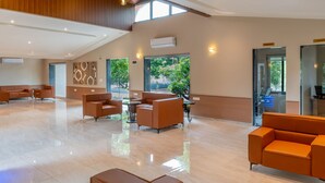 A spacious lobby with high ceilings, a polished floor, and orange seating areas. - Kings Kraft River Side Resort  (Talala)