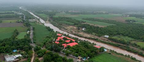 An aerial view of a rural area with fields, a river, and a cluster of buildings with red roofs.