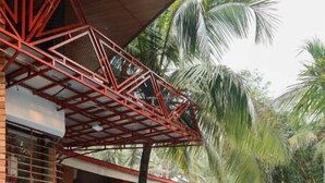Una piscina con solárium de baldosas, rodeada de palmeras y un edificio con estructura metálica roja.