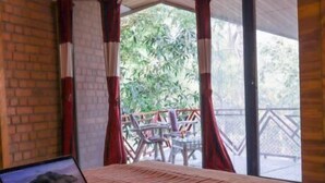 Un dormitorio con una laptop en la cama, una bandeja con tazas y vistas a un espacio exterior con sillas y una terraza de madera.