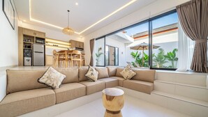 A modern living room with a sectional sofa, a wooden coffee table, and a kitchen area with built-in cabinets and a refrigerator.