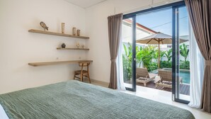 A bedroom with a bed, wooden shelves, a desk, and a view of an outdoor pool area.