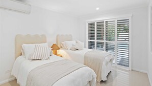 Een slaapkamer met twee bedden, een plafondventilator en een raam met zonwering.