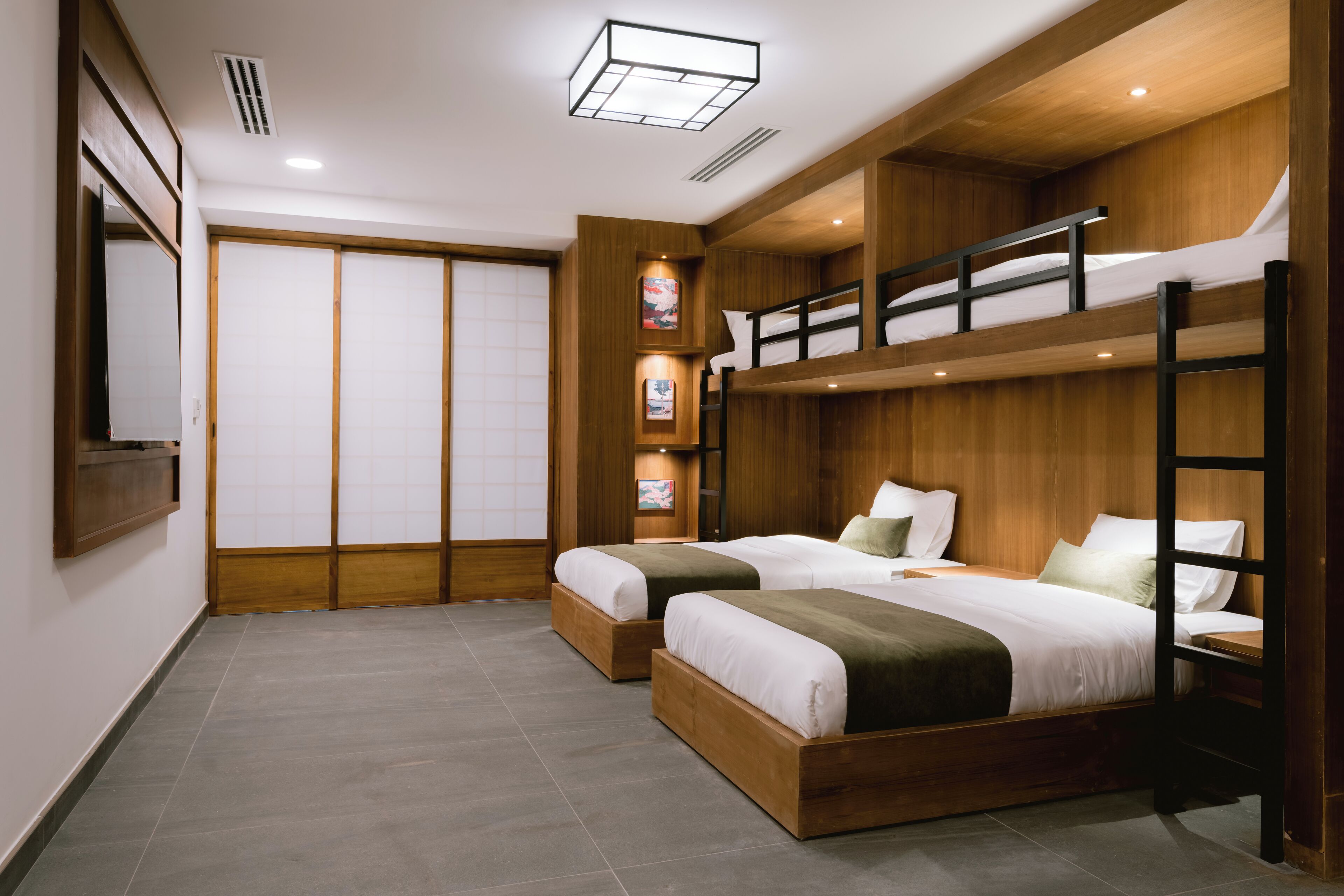 A hotel room with two bunk beds, wooden paneling, a sliding door, and a small shelf with pictures.