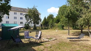 Un área de estar al aire libre con una mesa y sillas, una estructura verde y un edificio al fondo.