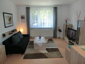 Ein Wohnzimmer mit einer Couch, einem Couchtisch, einem Fernseher und einem Fenster mit Vorhängen.