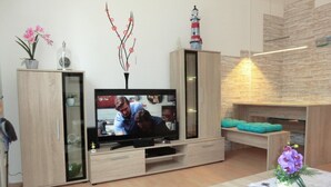 Una sala de estar con televisor, armarios de madera, chimenea y una mesa con un arreglo floral.