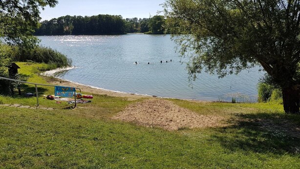 Vista a un lago con una playa de arena, una silla azul y una pequeña construcción.