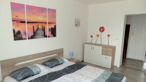 Un dormitorio con una cama, una mesita de noche, un aparador y un cuadro de un atardecer.