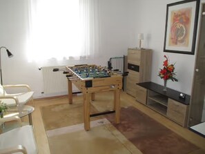 Une pièce avec un baby-foot, un radiateur, une chaise blanche, une petite table et un vase avec des fleurs.