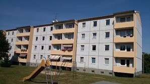 Un edificio residencial de varios pisos con balcones, un parque infantil y un cielo despejado.