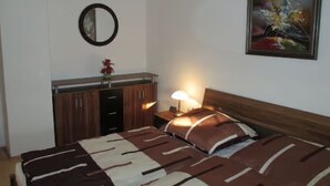 Un dormitorio con cama, mesita de noche con lámpara, espejo y un cuadro en la pared.