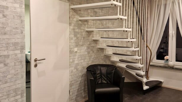 Un intérieur moderne avec un escalier en colimaçon, une porte, une chaise et une fenêtre avec des rideaux.