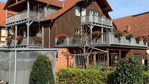 A multi-story wooden building with balconies, a brick facade, and a red-tiled roof.