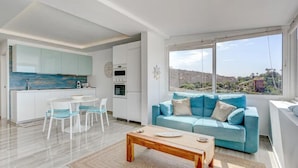 A modern living room with a blue sofa, a wooden coffee table, and a dining area with white chairs. - Ocean View Montesol Apartment with 2-bedrooms and outdoor swimming pool (Costa Adeje)