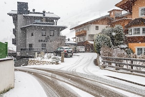 Une rue enneigée bordée d’immeubles, avec une voiture garée et une enseigne visible sur l’un des bâtiments.
