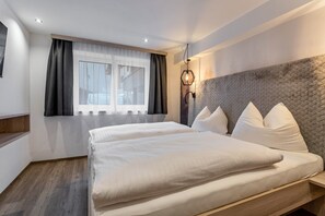 Une chambre d’hôtel avec un grand lit, une fenêtre avec des rideaux, une tête de lit agrémentée d’oreillers et un luminaire fixé au mur.