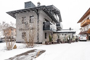 Moderni rakennus, jossa on kalteva katto, suuret ikkunat ja lumipeitteinen ajotie.