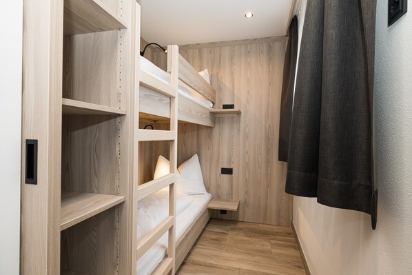 A room with bunk beds, a small shelf, and a curtain.