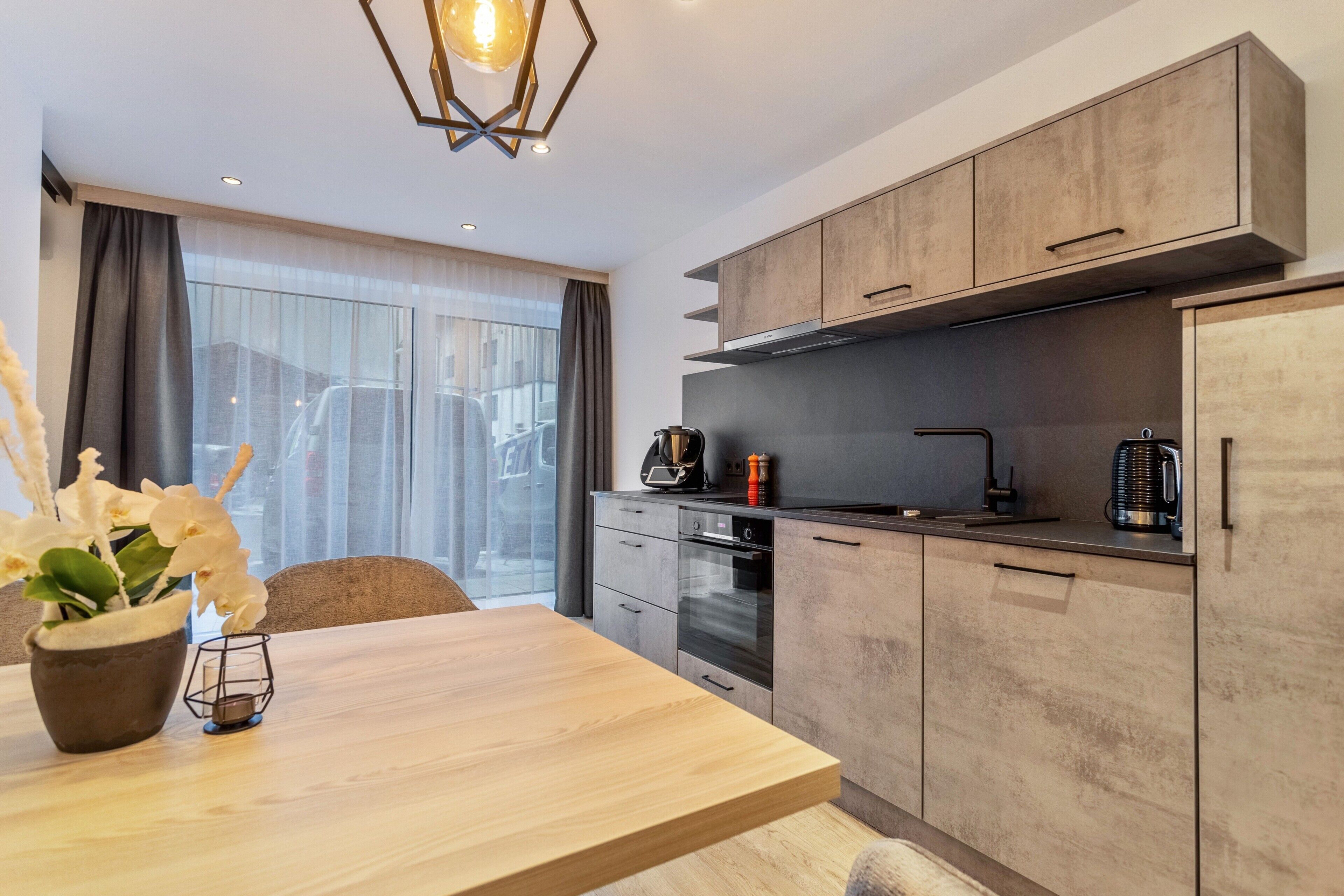 A modern kitchen with wooden cabinets, a built-in oven, and a dining area with a table and chairs.