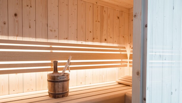 Un banc en bois pour sauna, accompagné d’un seau en bois et d’un porte-serviettes.