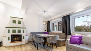 Un salon moderne avec une cheminée, une table à manger, des chaises grises, un canapé et une grande fenêtre.