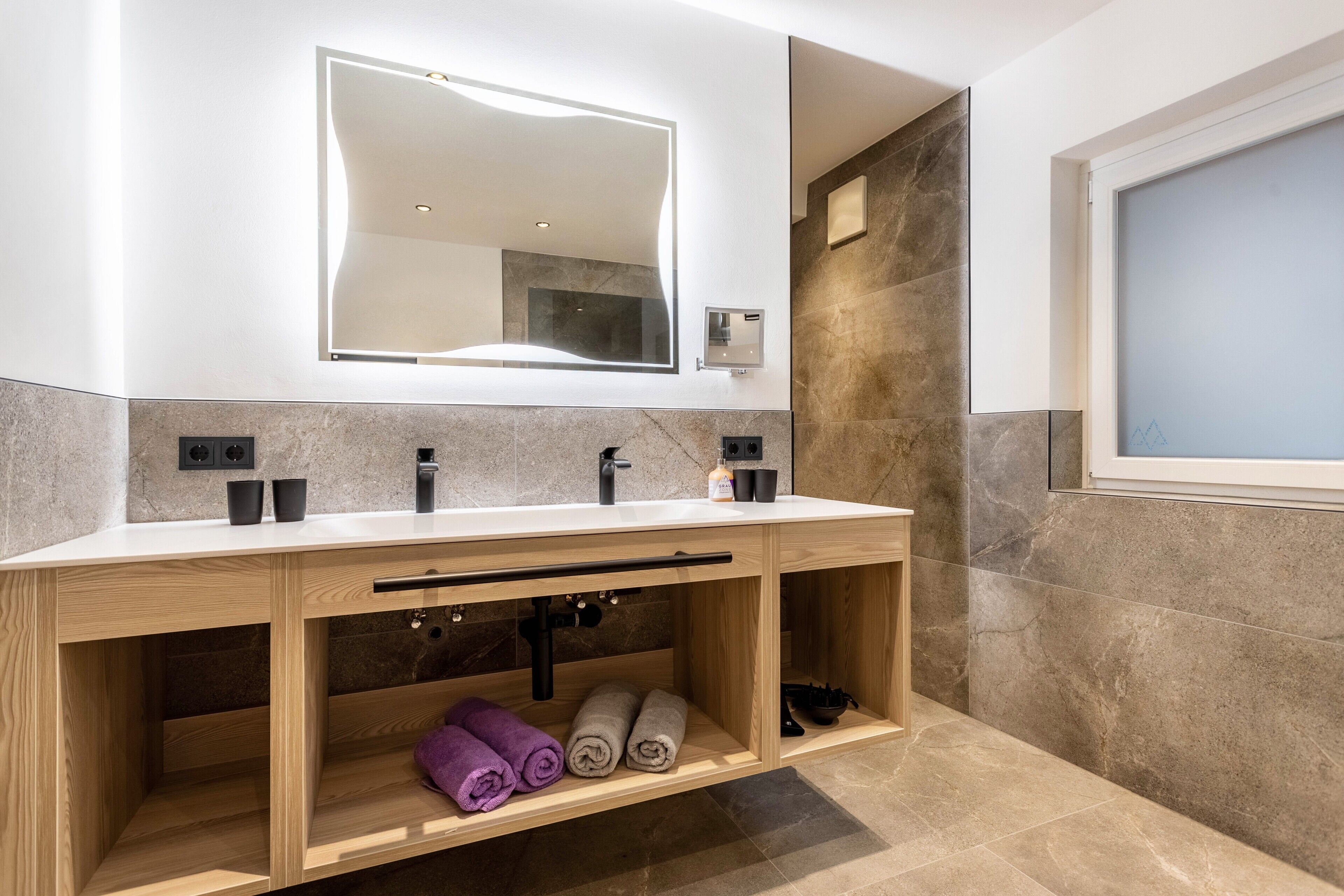 Une salle de bain moderne avec un double vasque, un grand miroir et un porte-serviettes intégré.