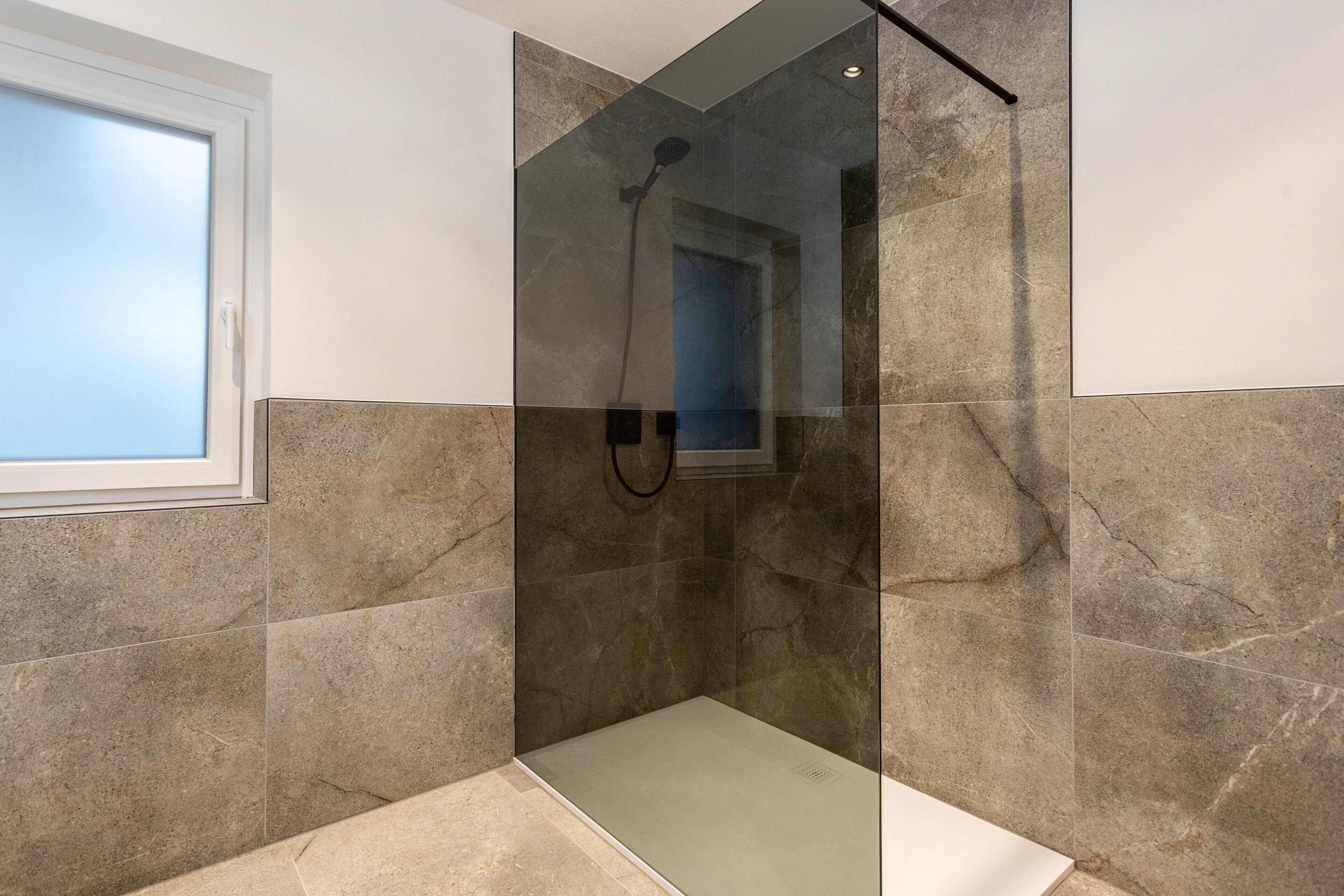 Un baño moderno con ducha envuelta en vidrio, paredes de mármol y ventana.