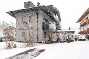 Un bâtiment moderne doté d’un toit en pente, de grandes fenêtres et d’une allée recouverte de neige.