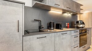 A modern kitchen with grey cabinetry, a stainless steel sink, a coffee maker, and a built-in oven.