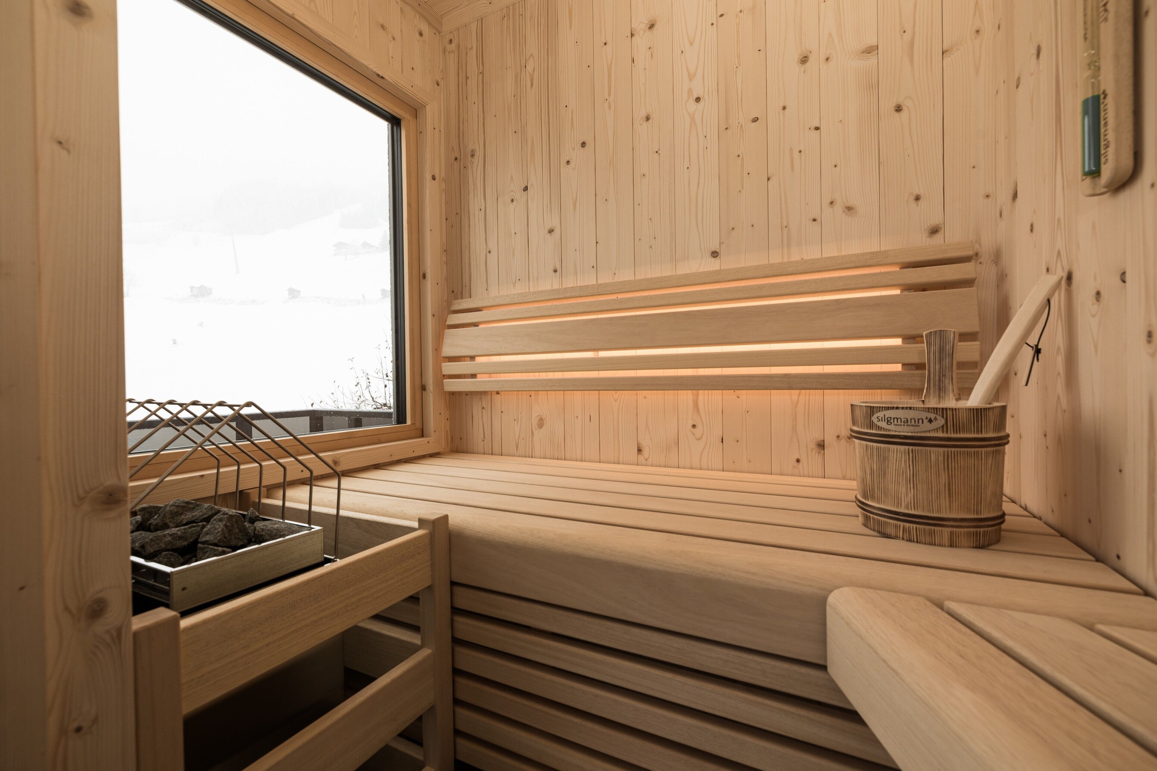 Una sala de sauna con listones de madera, una ventana y un balde de madera con la etiqueta 'slgmann'.
