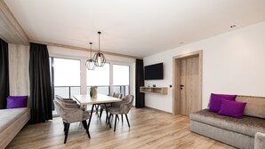 A modern living room with a dining area, a sofa, and a TV mounted on the wall.