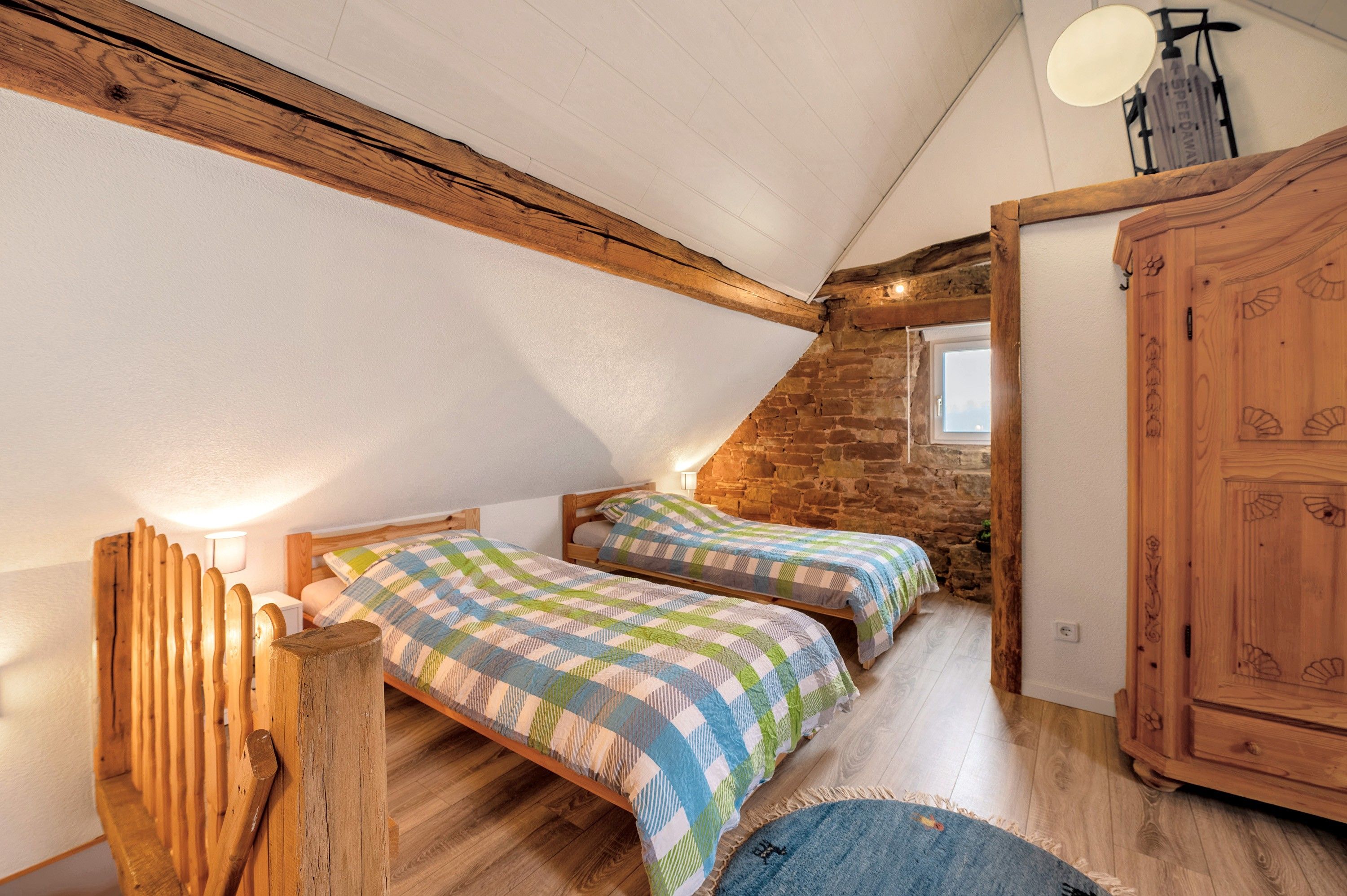 Ein gemütliches Schlafzimmer im Dachgeschoss mit zwei hölzernen Betten, einer Steinwand und einem Holzschrank.