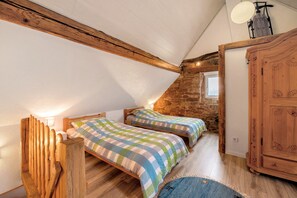 A cozy attic bedroom with two wooden beds, a stone wall, and a wooden wardrobe.