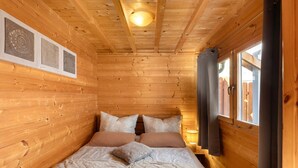 Habitación de cabaña de madera con cama, lámpara de techo y ventana con cortinas.
