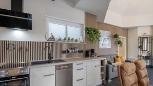 A modern kitchen with built-in appliances, a dining area with a sofa, and a living room with a brown leather chair. - Holiday Home Seepanorama - Marina Mücheln with Lake View, Private Terrace & Wi-Fi (Mücheln (Geiseltal))